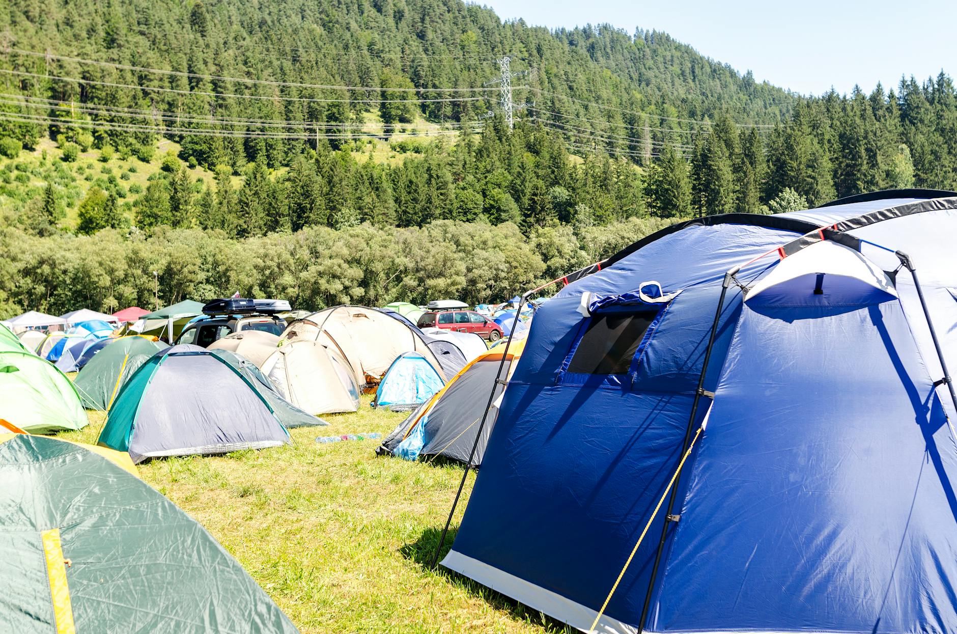 Tents set in a lush green valley with a forested mountain backdrop under a clear sky.