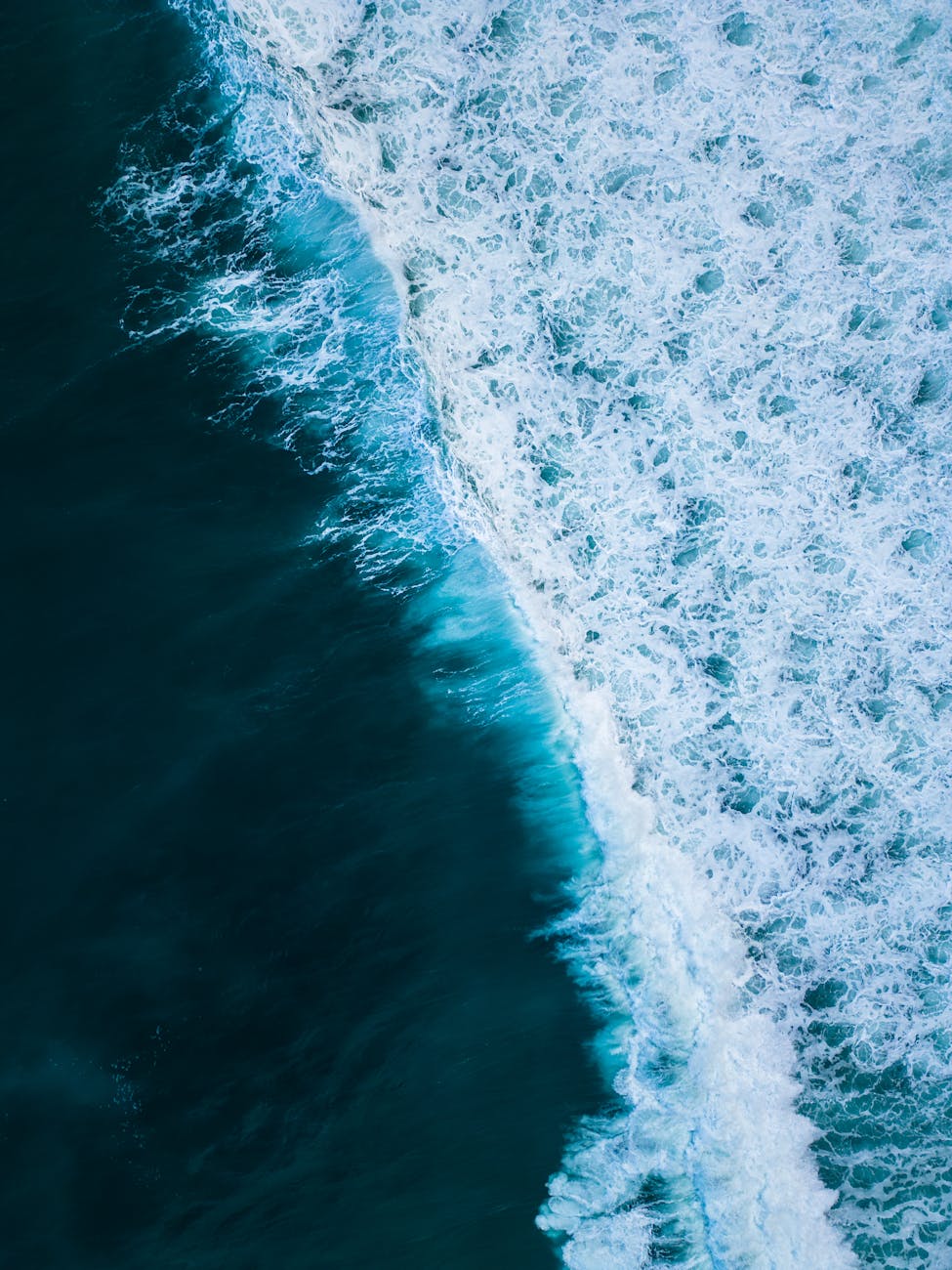 Vivid aerial view of ocean waves crashing onto the shoreline, capturing the dynamic scene from high above.