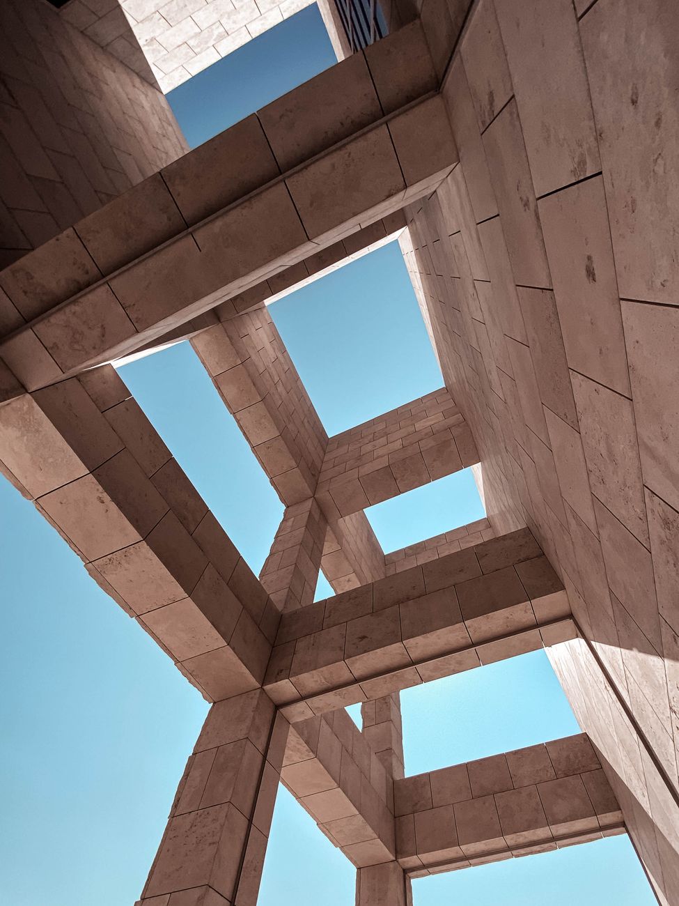 Upward view of modern geometric architecture with clear blue sky.