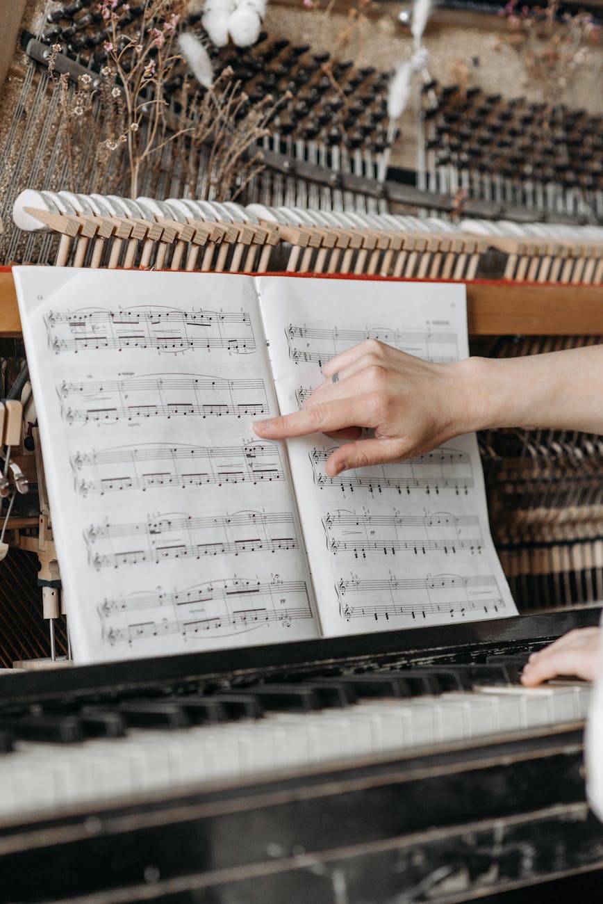 Close-up of a hand pointing at sheet music on a piano, highlighting musical notes.
