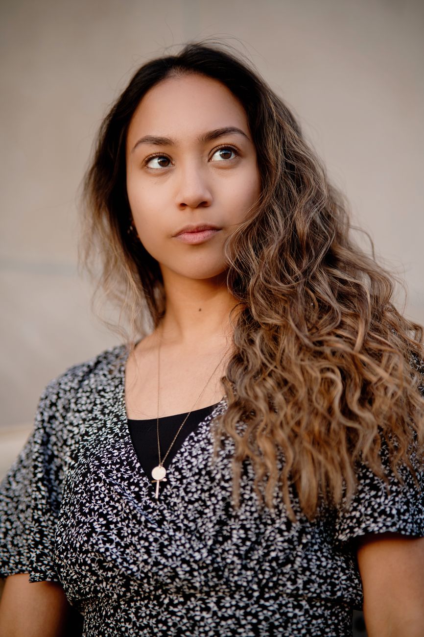 An outdoor portrait of a beautiful woman with long curly hair and a thoughtful expression.