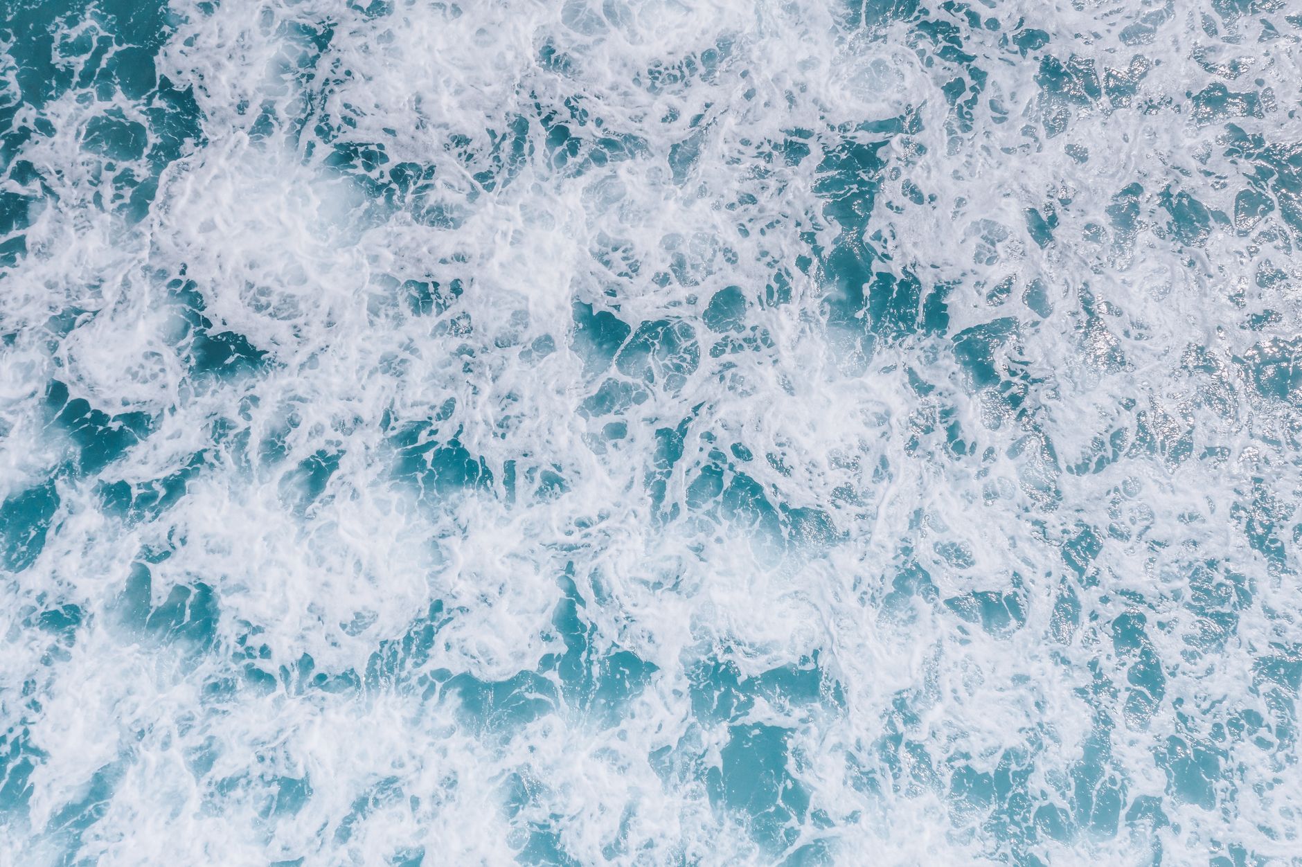 A dynamic top view of ocean waves and sea foam demonstrating nature's power and beauty.