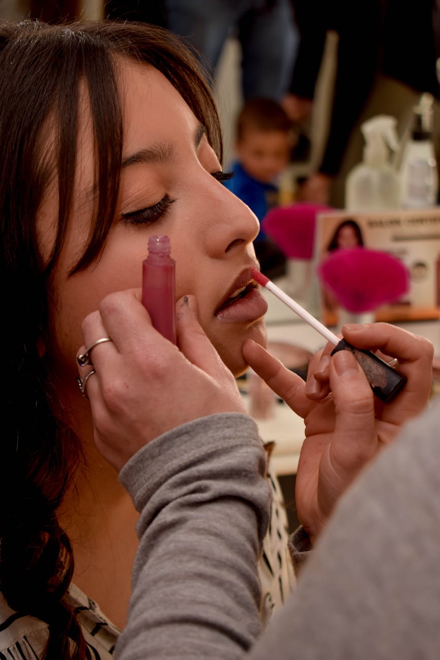 Close-up of a makeup artist applying lipstick to a woman in a salon setting.