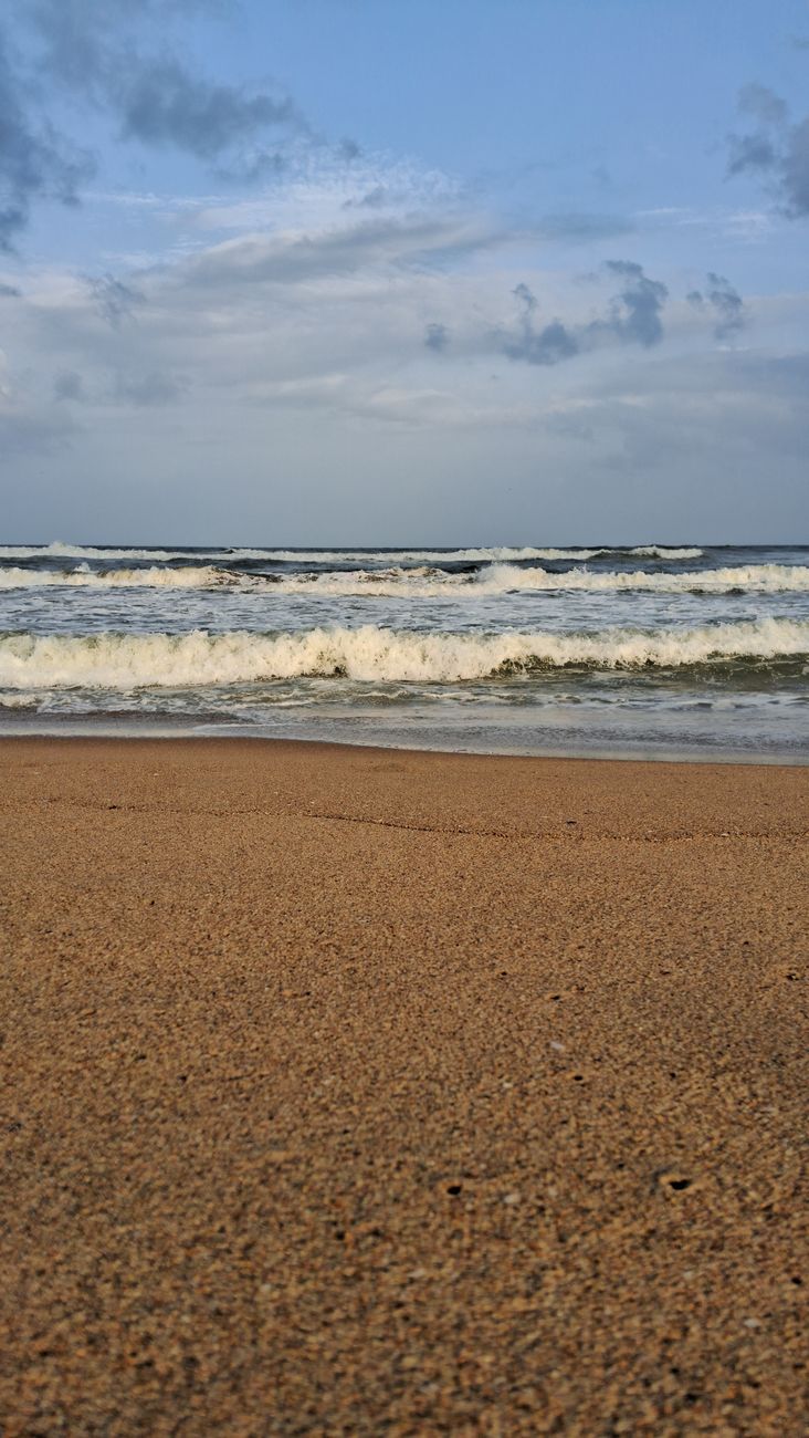 Tranquil view of gentle ocean waves lapping a sandy beach under a clear blue sky.