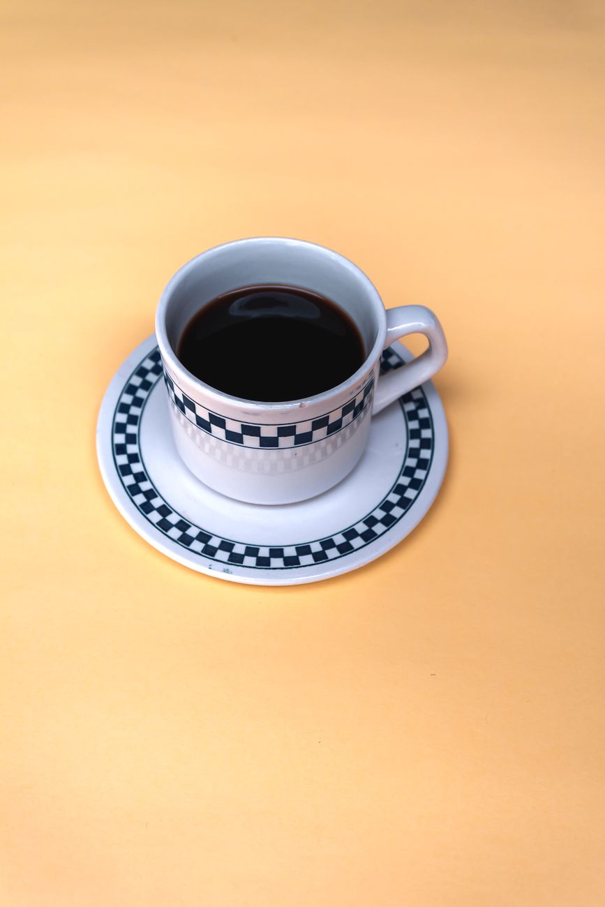 Elegant ceramic teacup with checker pattern on a vibrant yellow background, perfect for beverage themes.