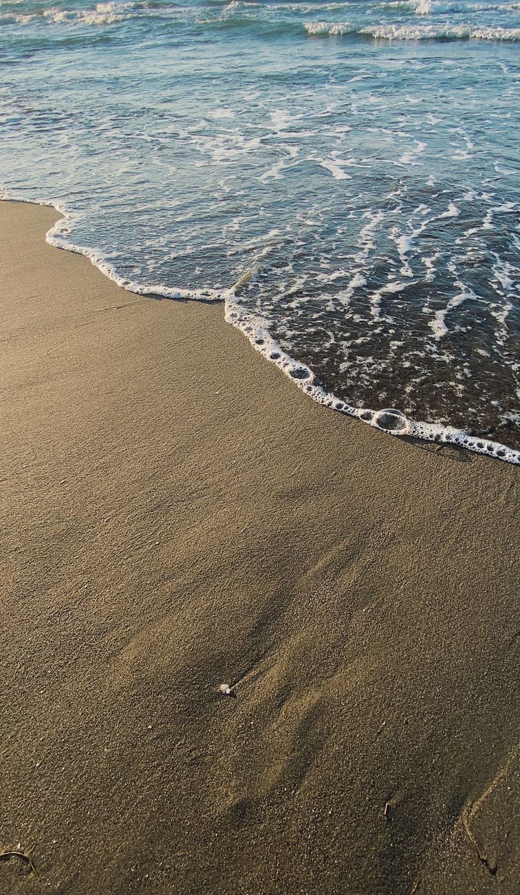 Calm ocean waves meet golden sandy beach at sunset, creating a tranquil coastal scene.