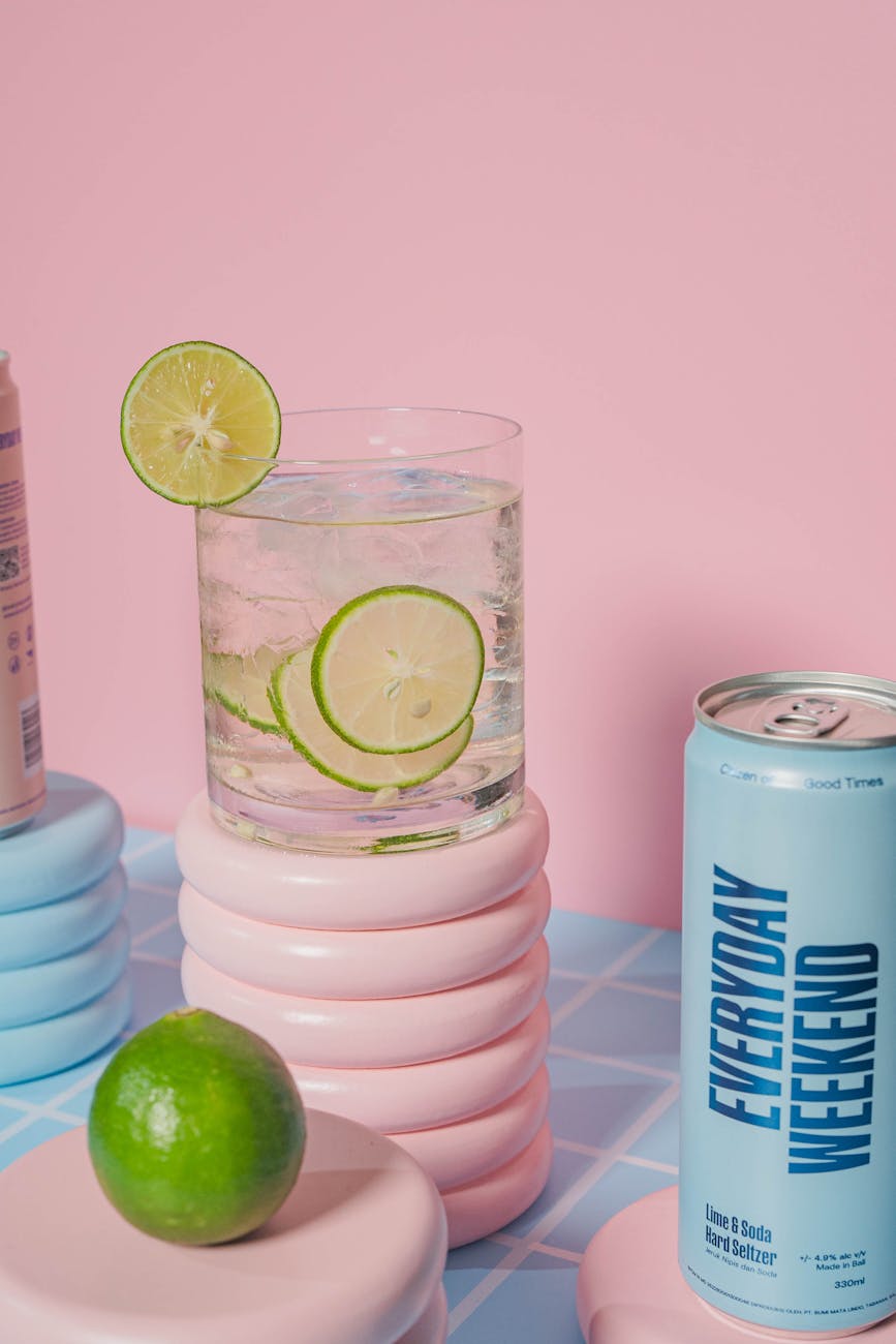 A refreshing lime soda in a glass with lime slices, set against a pink background.
