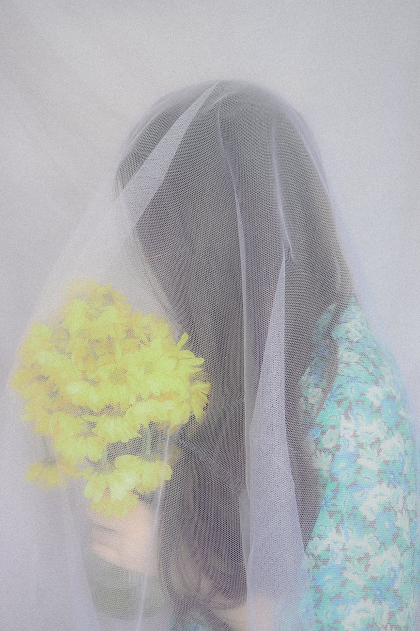 Artistic portrait of a bride with a bouquet under a soft veil, exuding dreamy elegance.