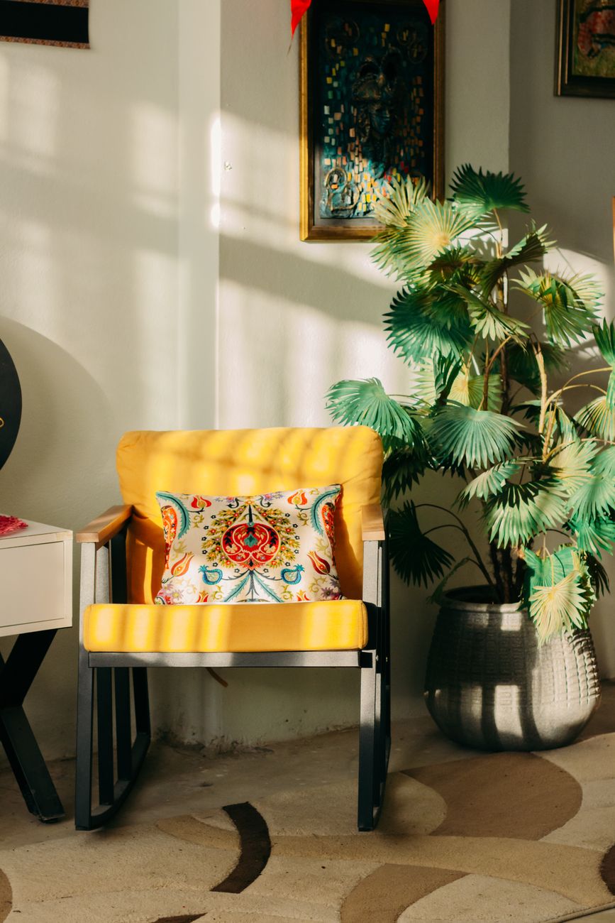 Bright interior featuring a yellow chair, patterned pillow, and potted plant.