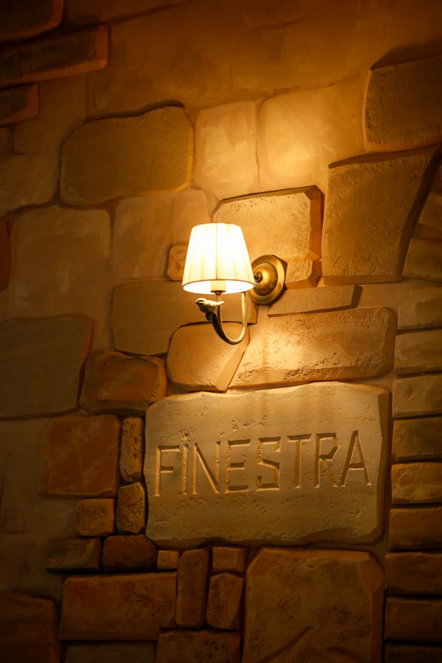 A cozy wall sconce light illuminates a textured wall with 'Finestra' inscription.