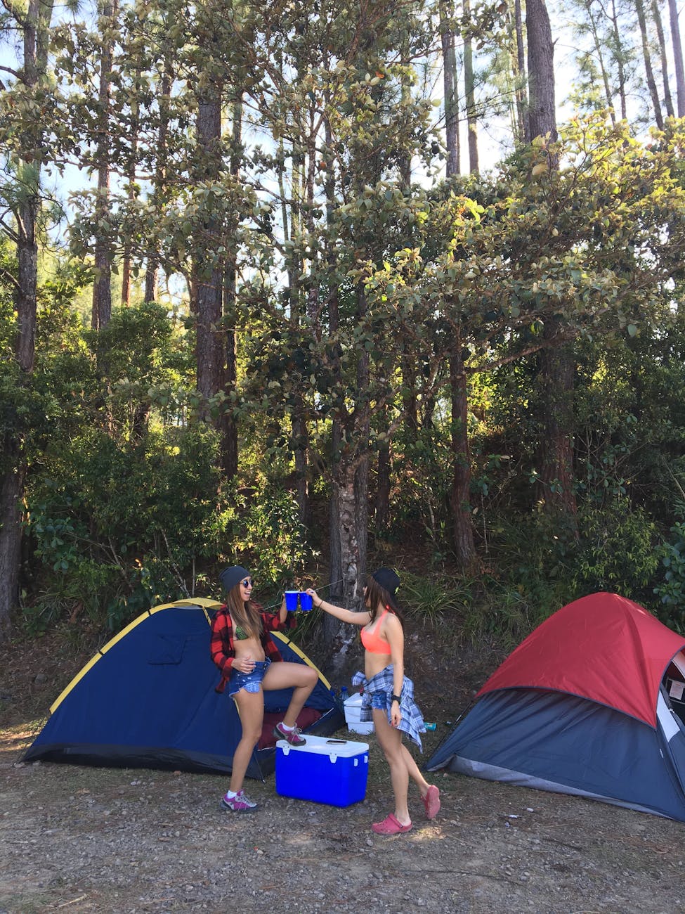 Two women enjoying a camping trip in a forest in Panama with tents and a cooler.