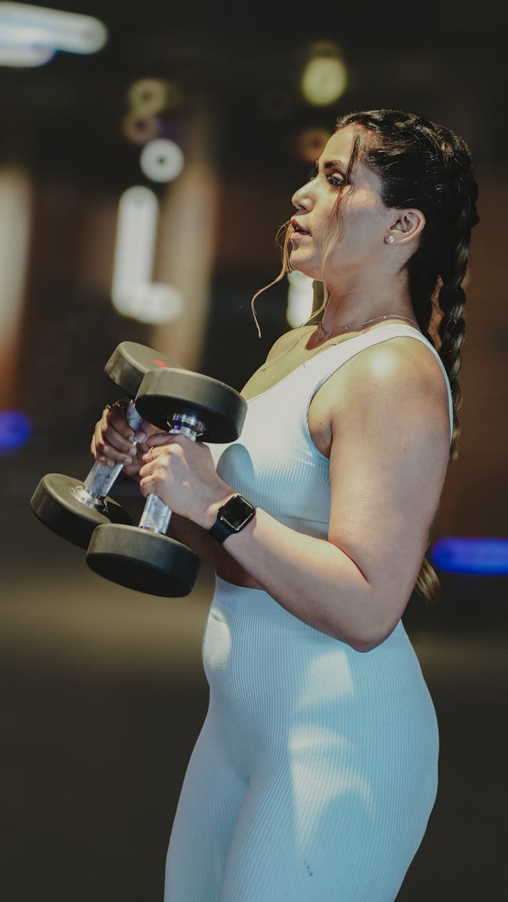 A focused woman lifting dumbbells during a workout in a gym, showcasing strength and fitness.