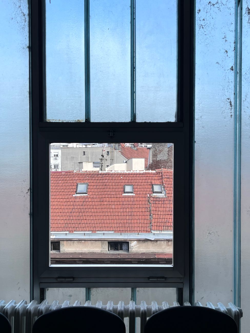 Red tile roof seen through a large window in an urban setting.