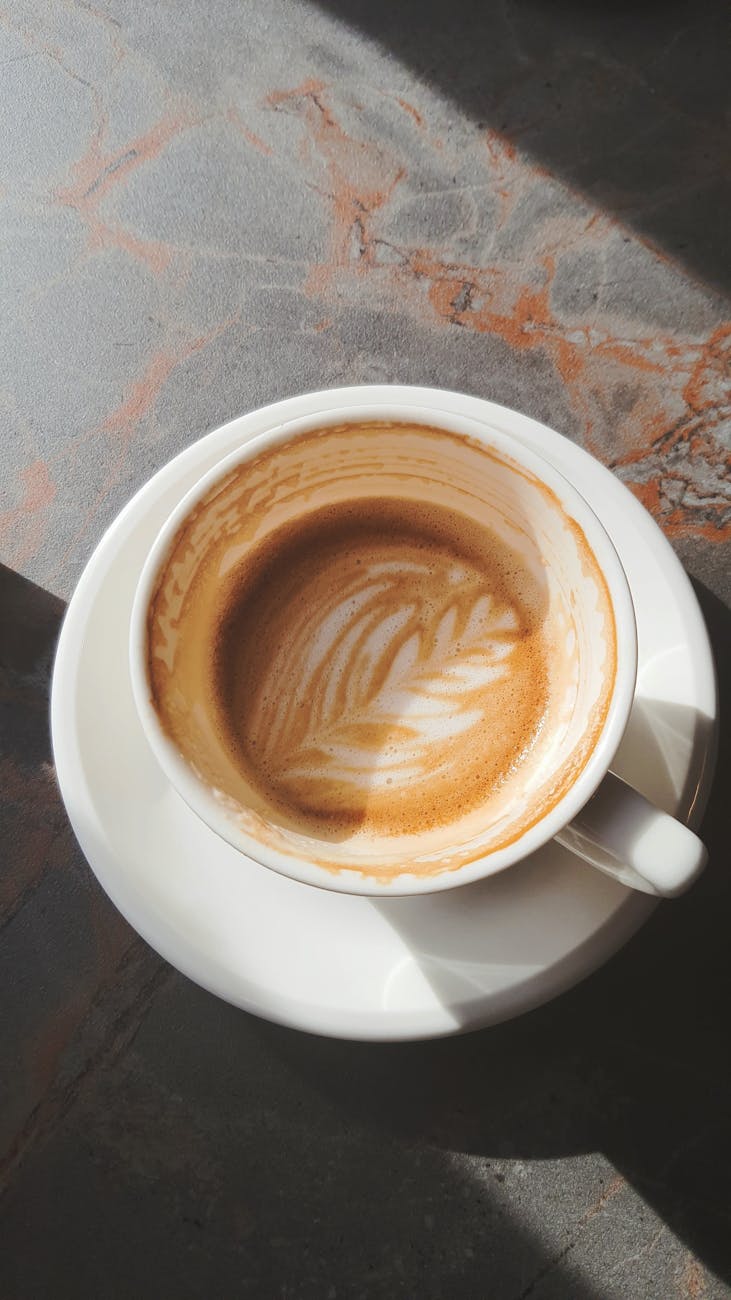 A close-up of intricate coffee art in a white cup, highlighting latte art foam in natural light.