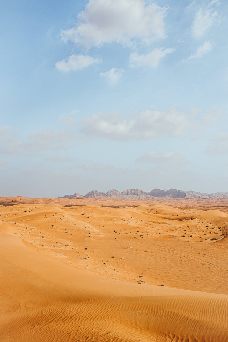 Explore the serene expanse of Dubai's desert, showcasing vast sand dunes and distant mountains under a blue sky.