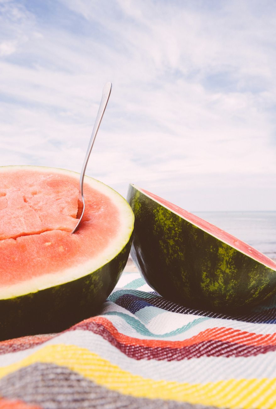 Juicy watermelon halves on a striped blanket at the beach, perfect for summer refreshment.