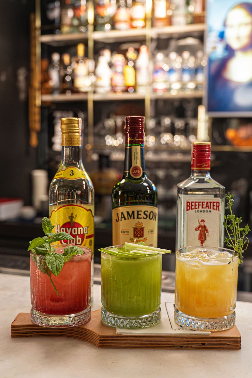 Vibrant cocktails with garnish displayed in a stylish bar, featuring Havana Club, Jameson, and Beefeater bottles.