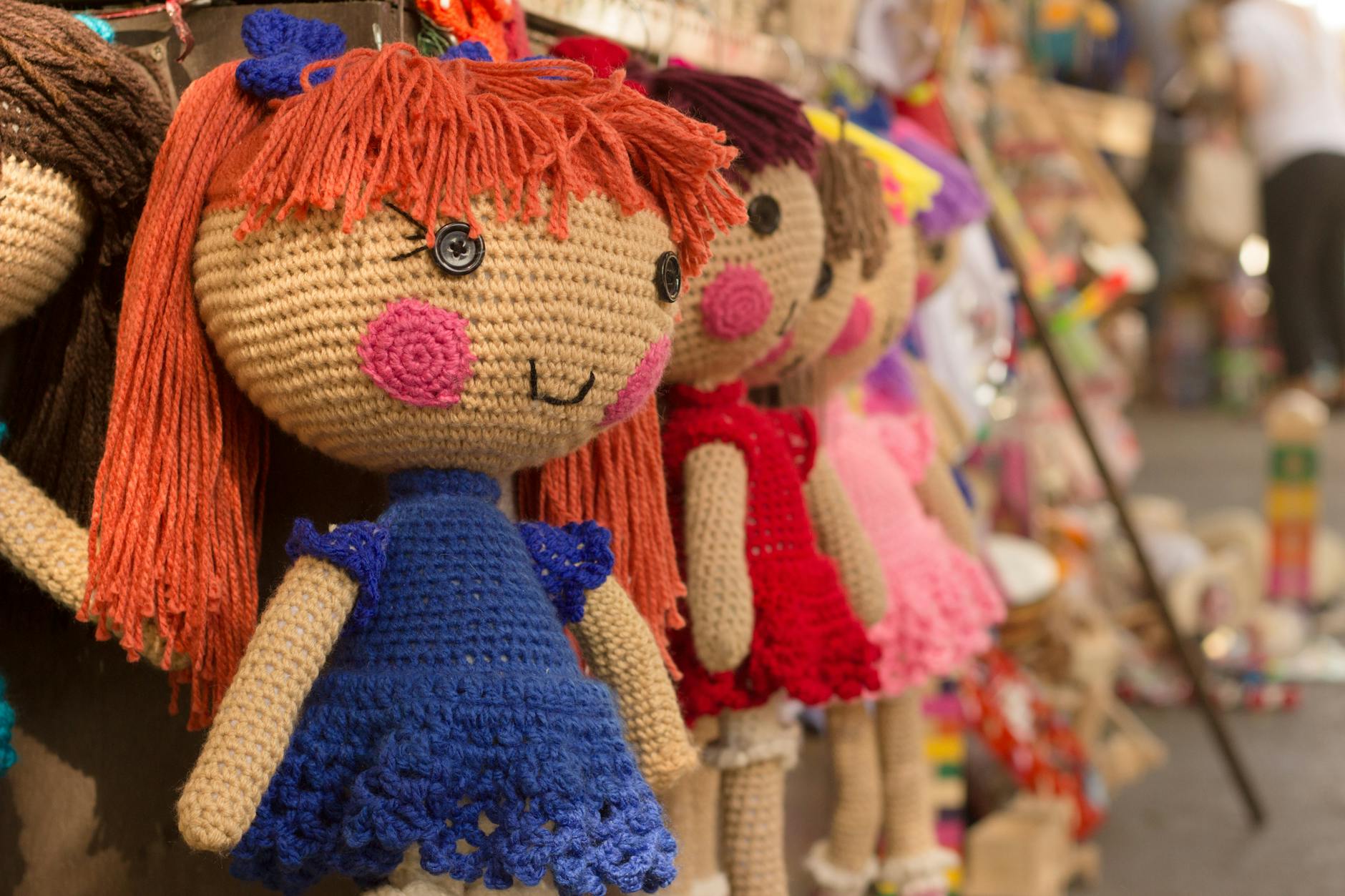 Charming crocheted dolls in bright clothes hang at a market stall.