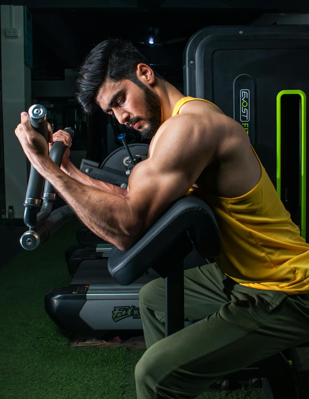 Muscular man in a gym performing bicep curls on a machine, showcasing strength and dedication.