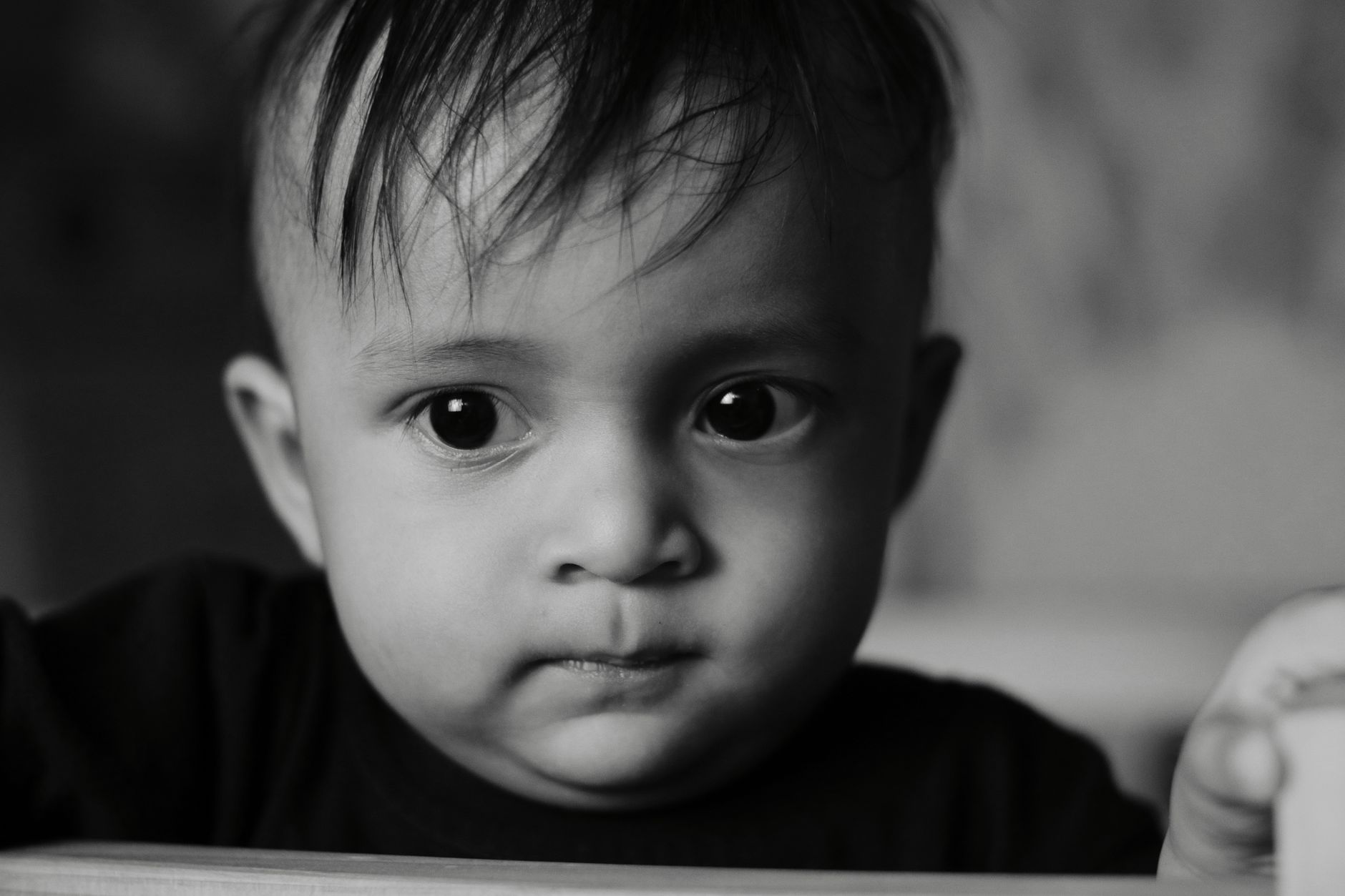 A close-up black-and-white portrait capturing the curious expression of a toddler indoors.