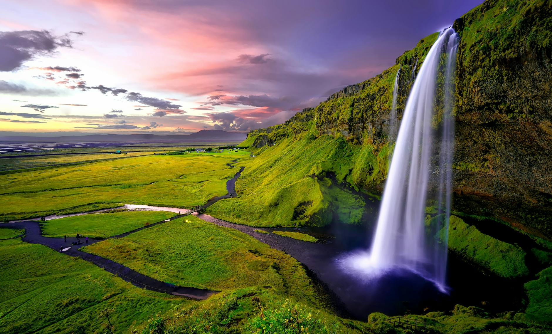 Stunning waterfall cascading over green cliffs during a vibrant Icelandic sunset.