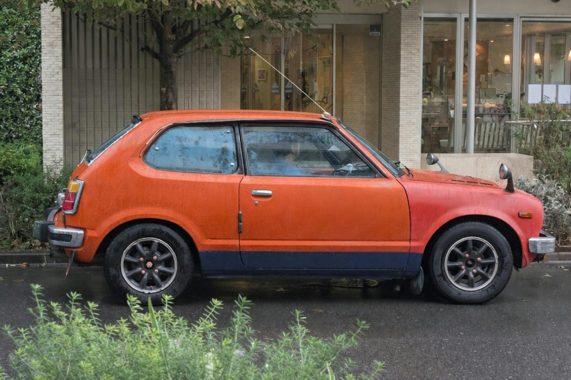 Classic orange hatchback car parked outdoors on a wet street in Tokyo, Japan.