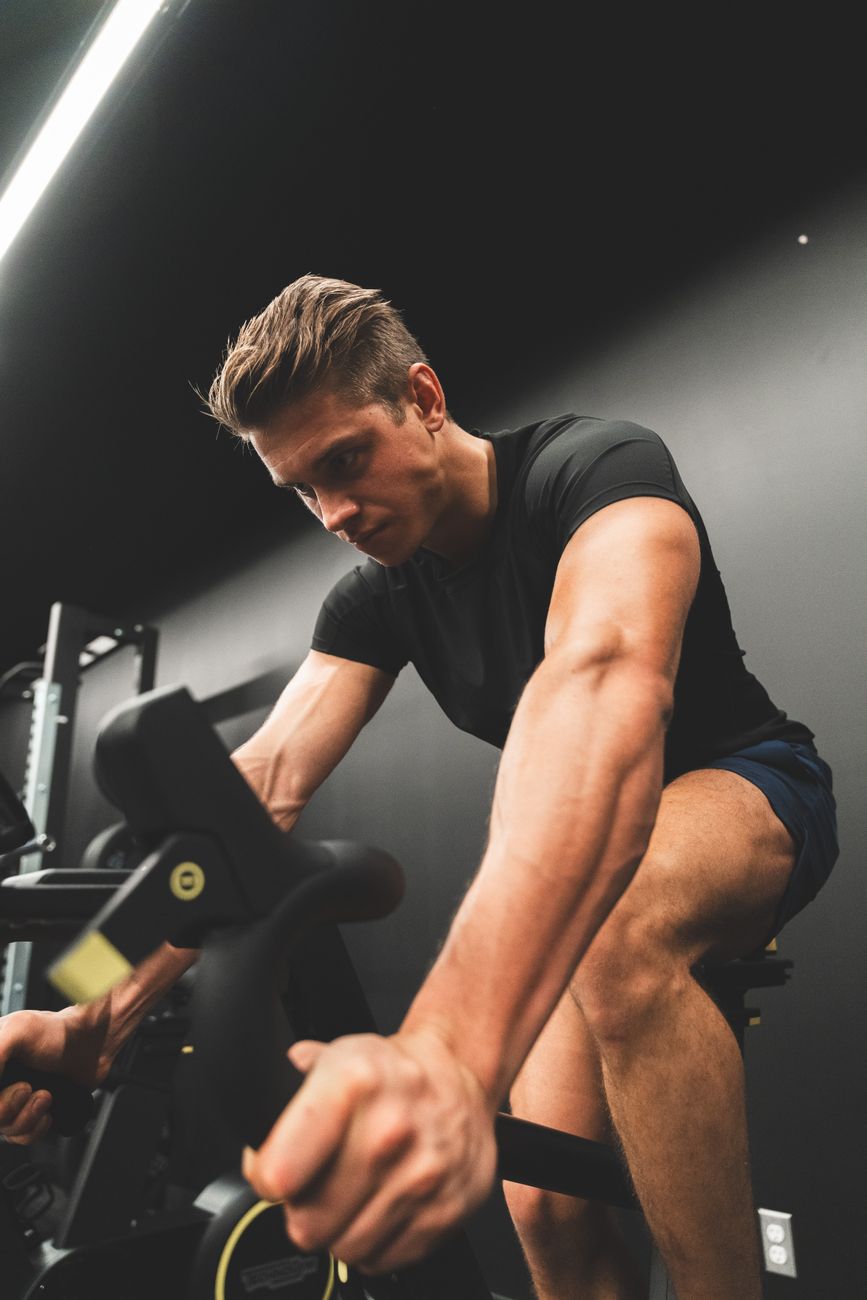 Fit young man intensely cycling on a stationary bike indoors.