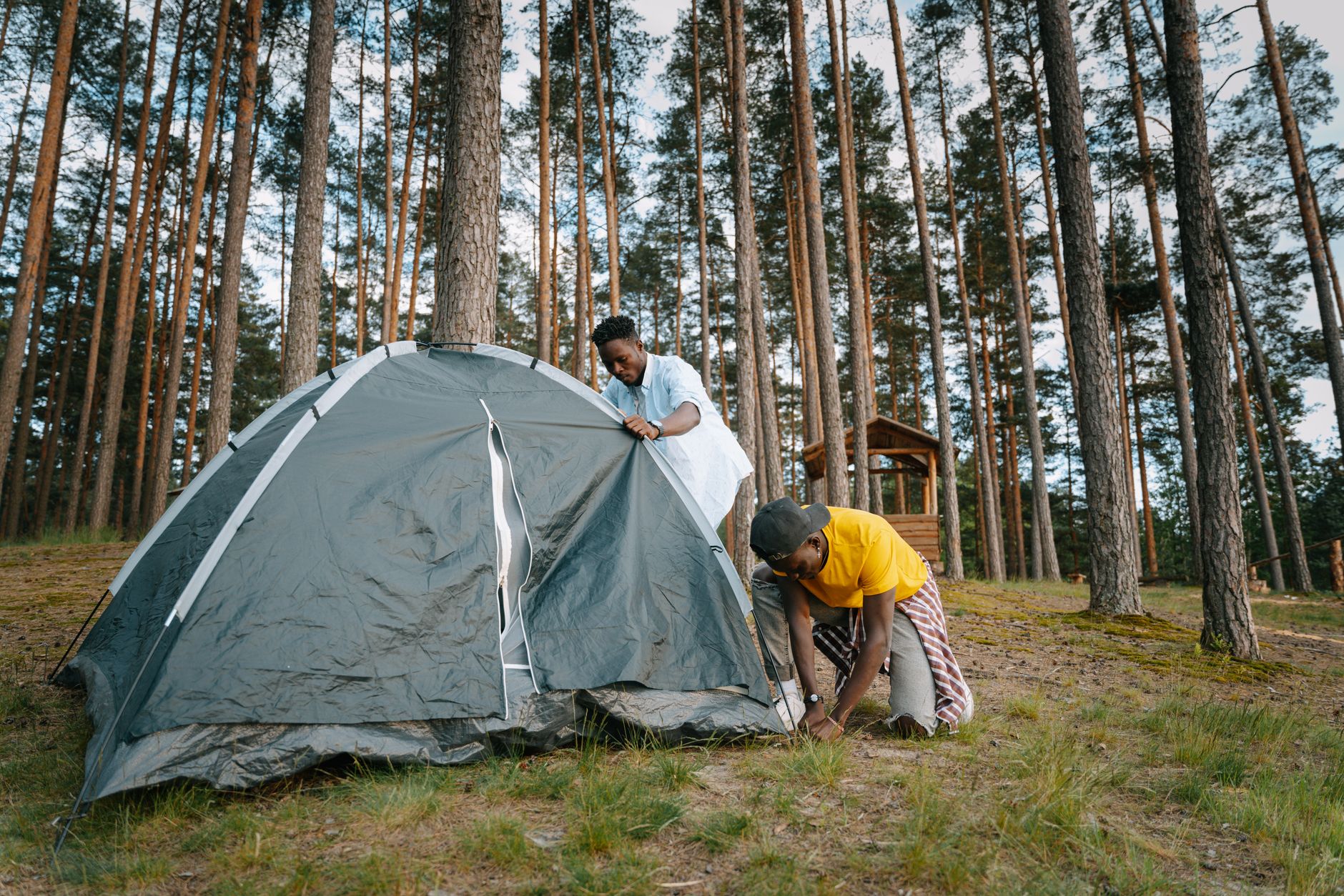 Two men assembling a tent in a forest campsite, enjoying an outdoor adventure.