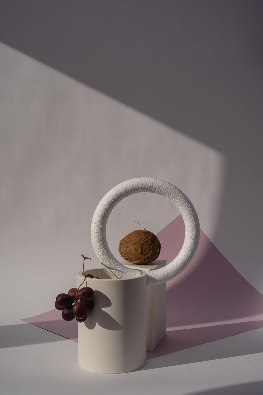 A minimalist composition featuring a coconut and grapes in geometric shapes with soft lighting.