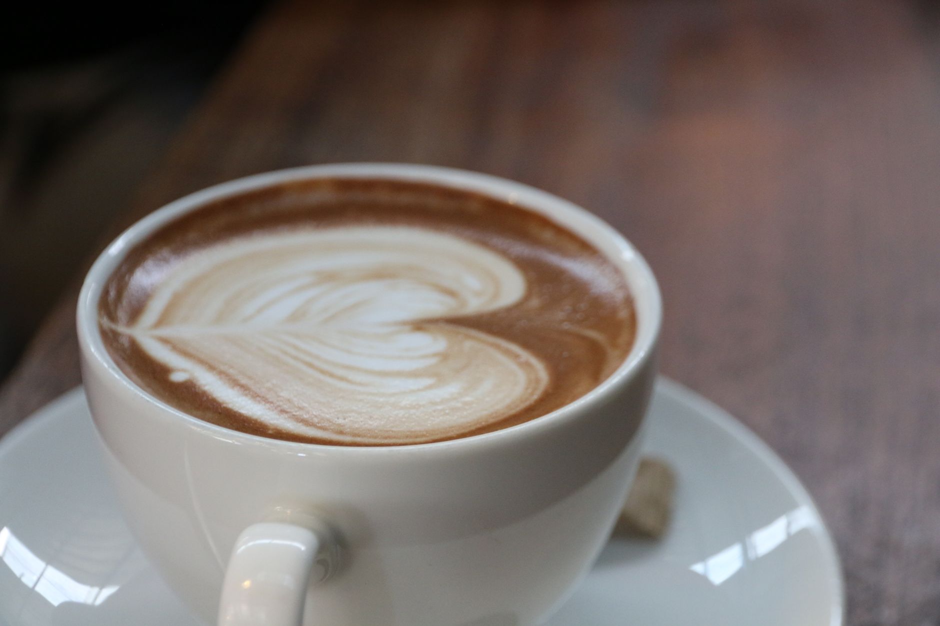 Close-up of a latte with heart-shaped art in a white cup on a wooden table.