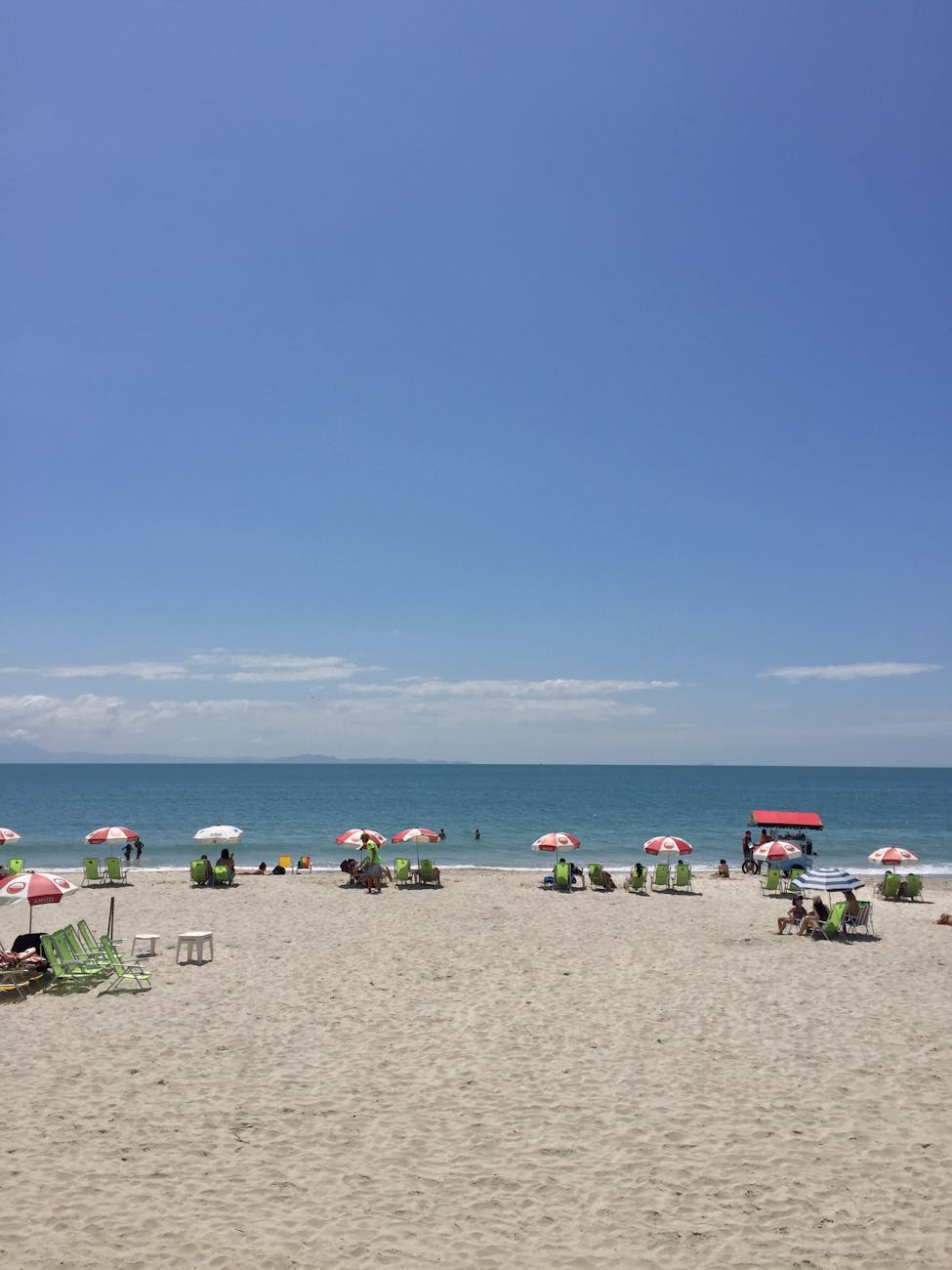 A vibrant beach scene with umbrellas and sunbathers enjoying a beautiful summer day by the ocean.