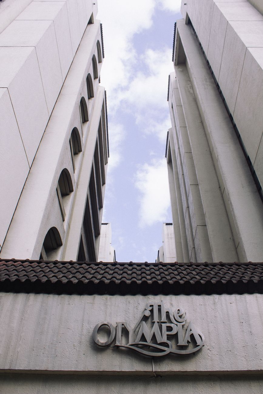 Low angle view of The Olympia building with dramatic sky backdrop.