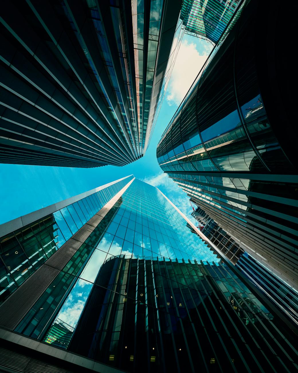 Low-angle view of modern skyscrapers reflecting the blue sky in a bustling urban area.