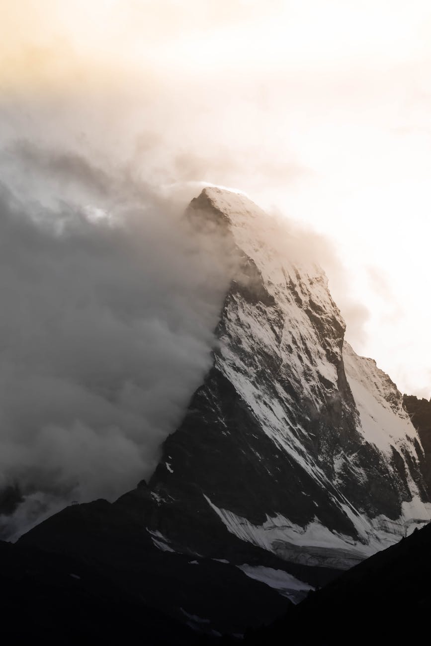 Dramatic view of snow-covered Matterhorn peak piercing clouds at sunrise in Zermatt, Switzerland.
