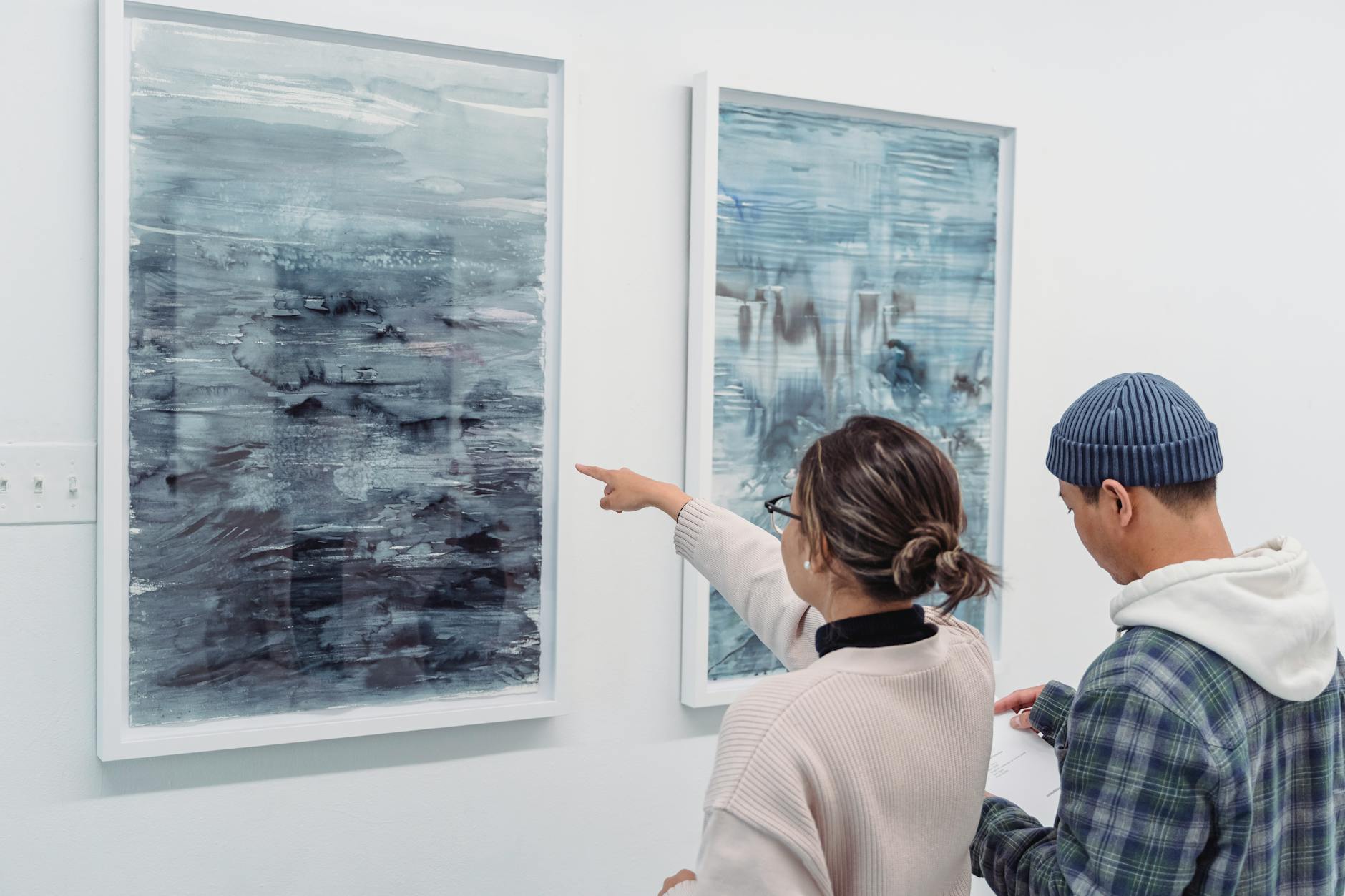 Two people examining abstract artwork in a gallery, engaging with the art.