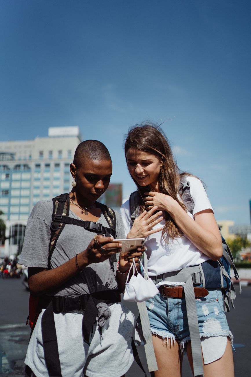 Two women travelers exploring a city using a smartphone, one African American and one Caucasian.