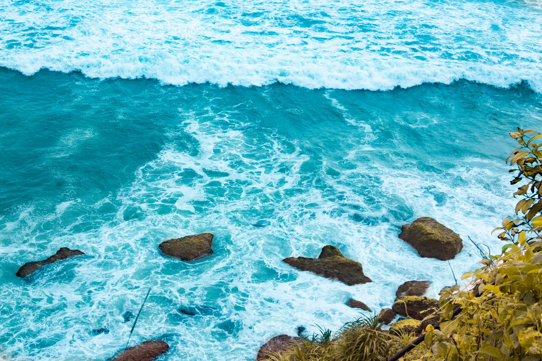 High angle view of turquoise ocean waves crashing on rocks. Perfect for travel and nature themes.