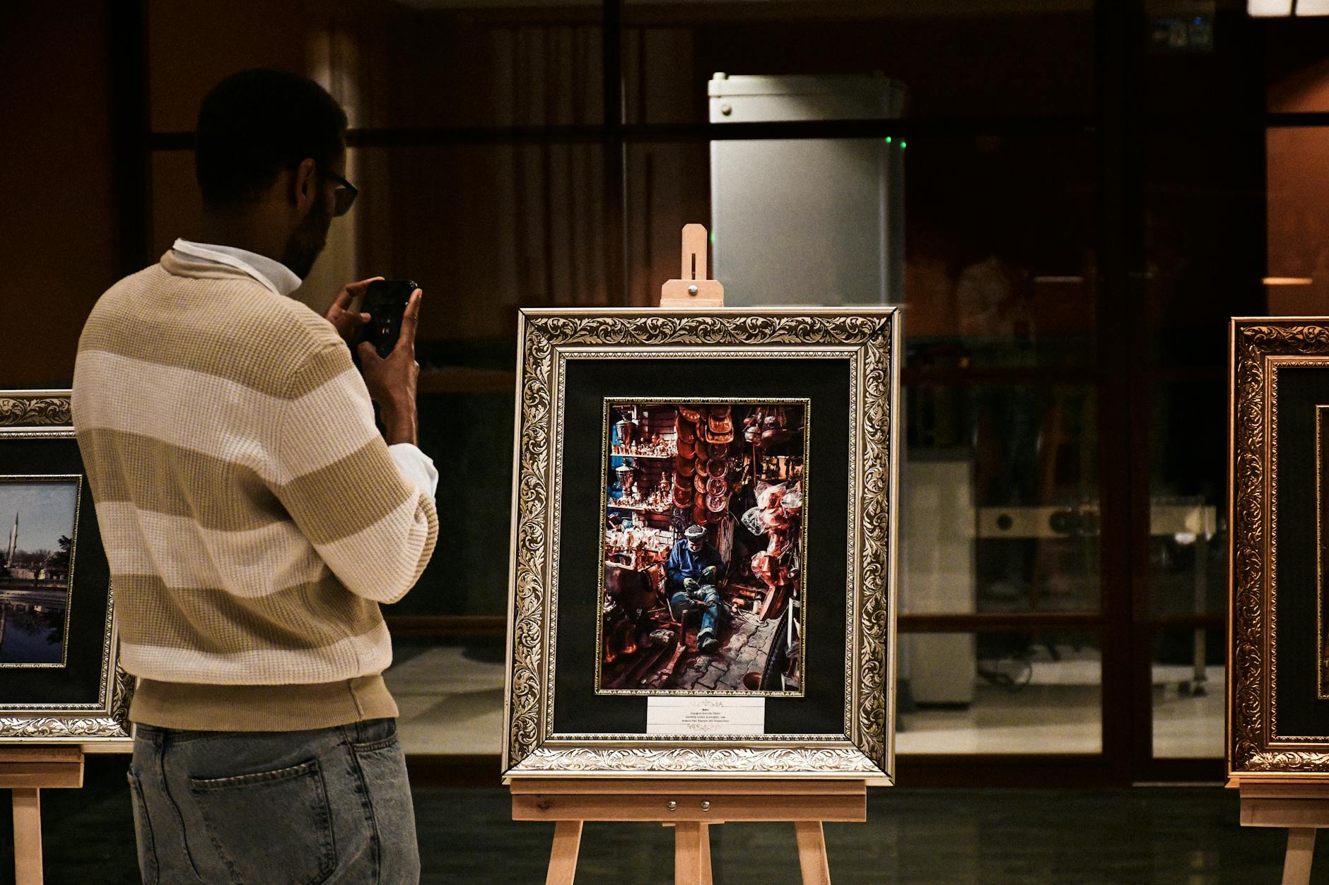 A man photographs art pieces in a modern indoor gallery setting.