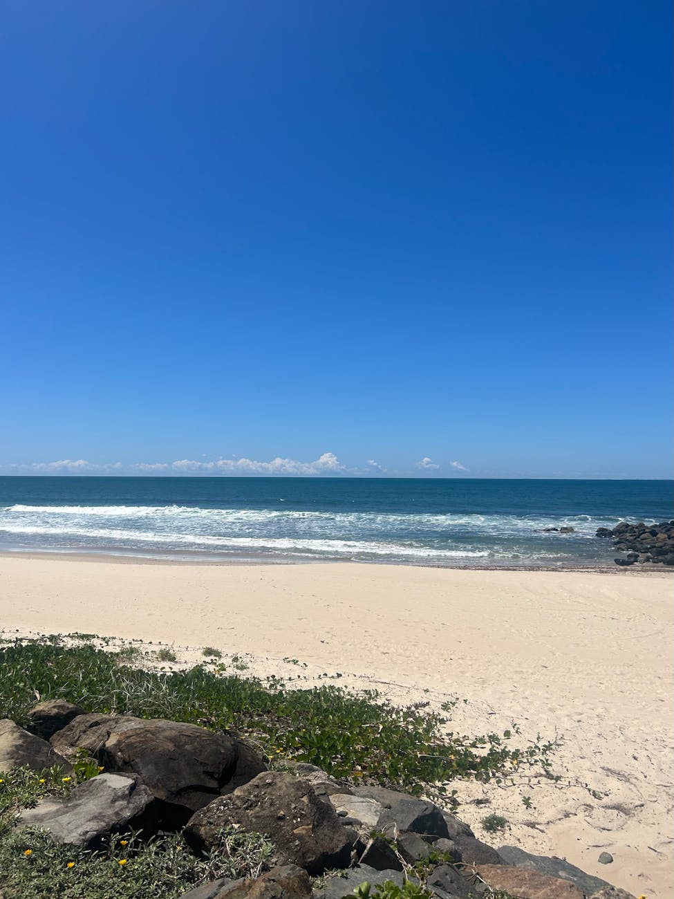 Peaceful sandy beach at Sunshine Coast, Australia, under a clear blue sky and gentle ocean waves.