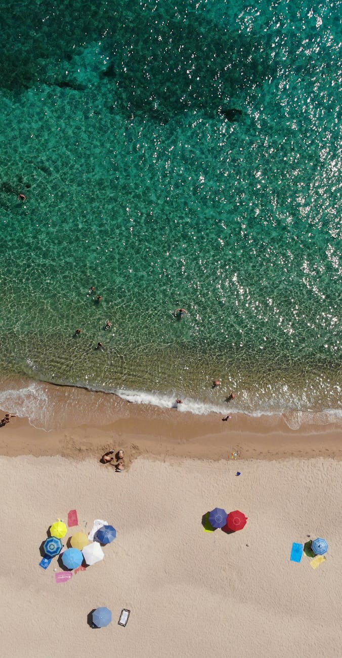 Aerial view of colorful umbrellas on Geremeas Beach, Sardinia's pristine shoreline.