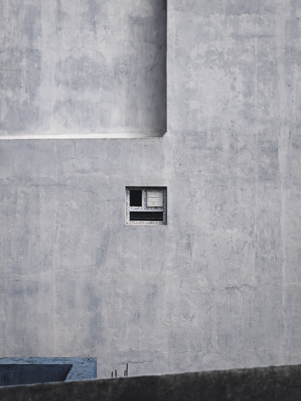 A small window on a large, concrete wall showcasing minimalist architecture in Chennai, India.