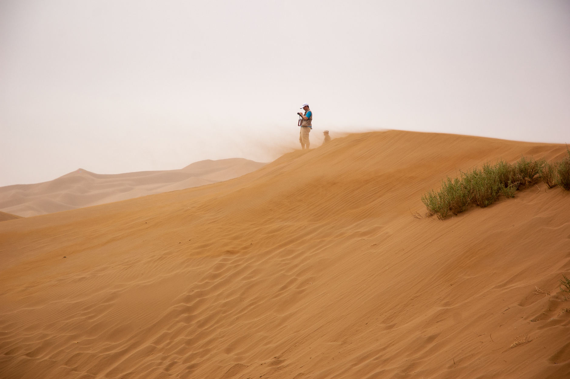 A lone traveler stands atop sand dunes in an expansive desert landscape, enjoying a summer adventure.