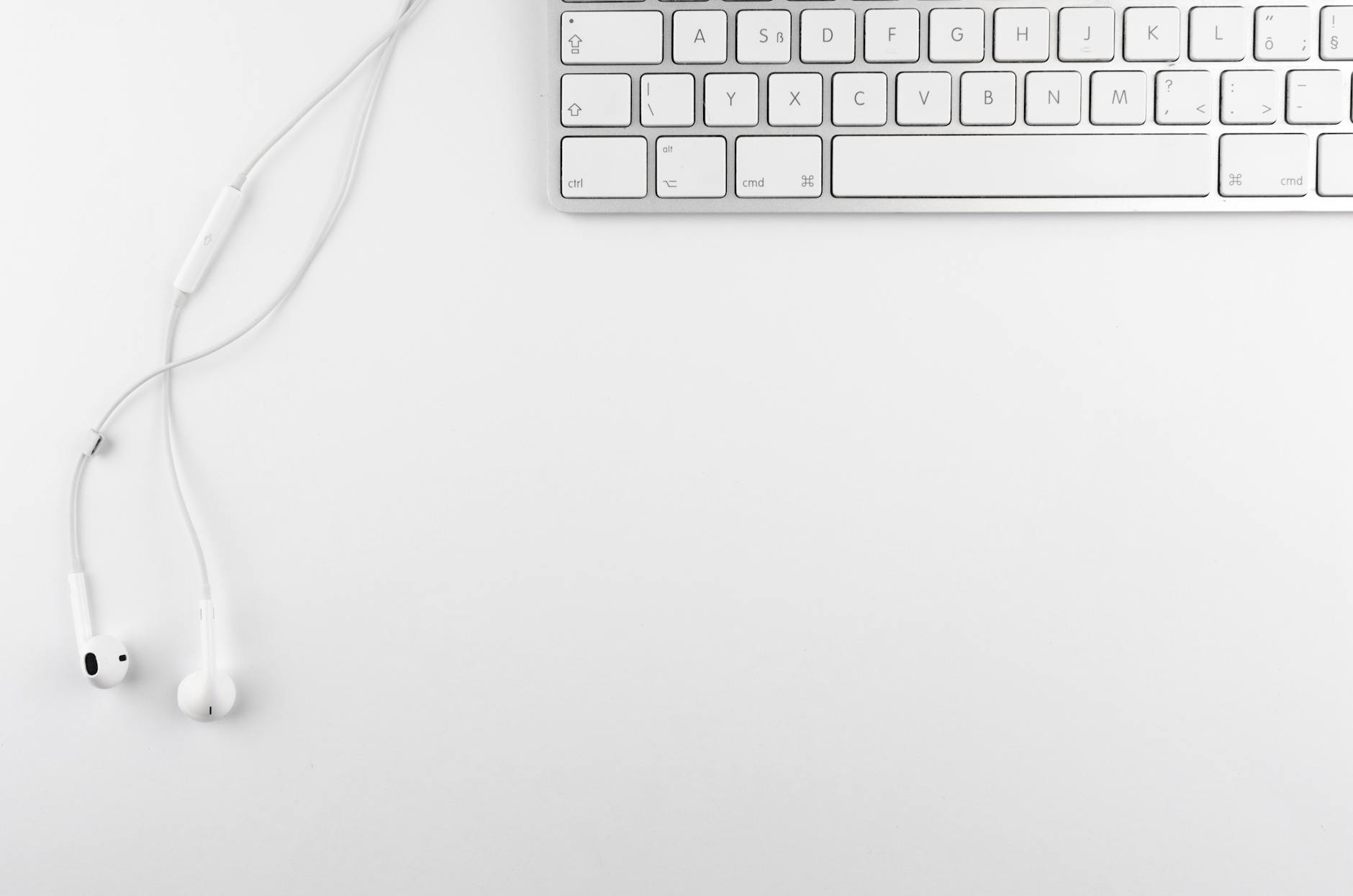 Top view of a minimal white desk setup featuring a keyboard and earphones on a clean background.