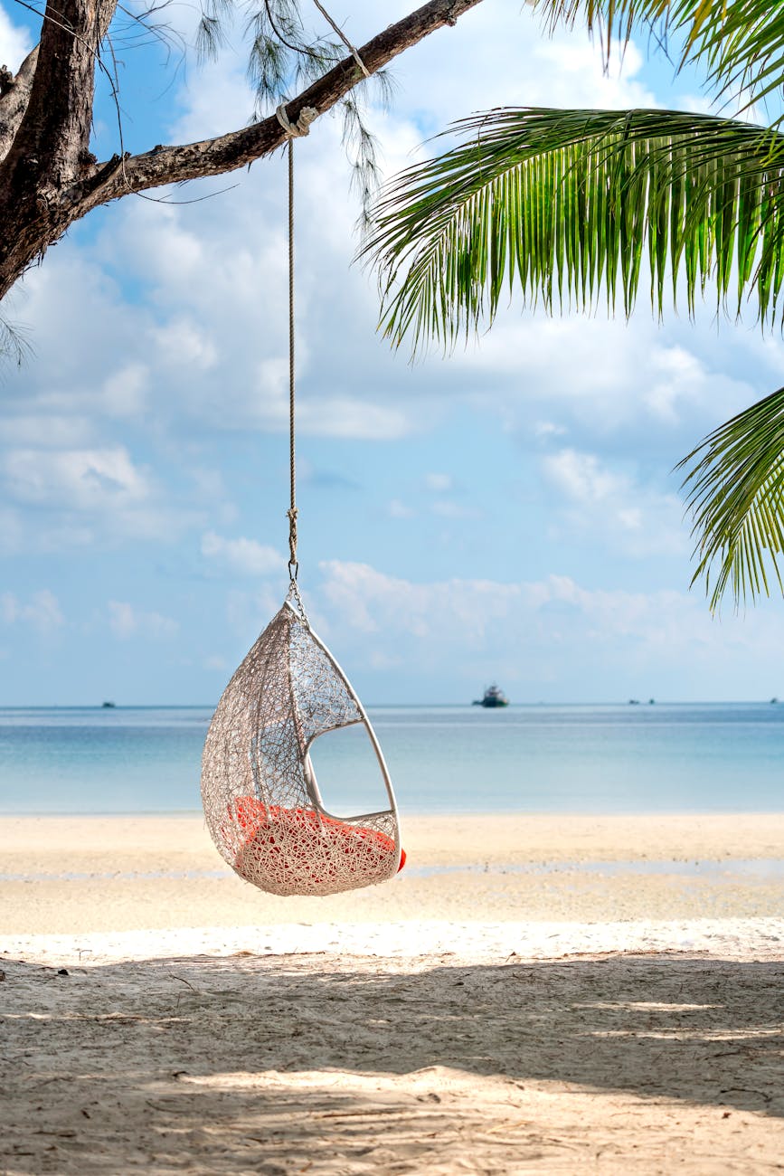 A peaceful scene with a hanging swing chair on a tropical beach, perfect for relaxation.