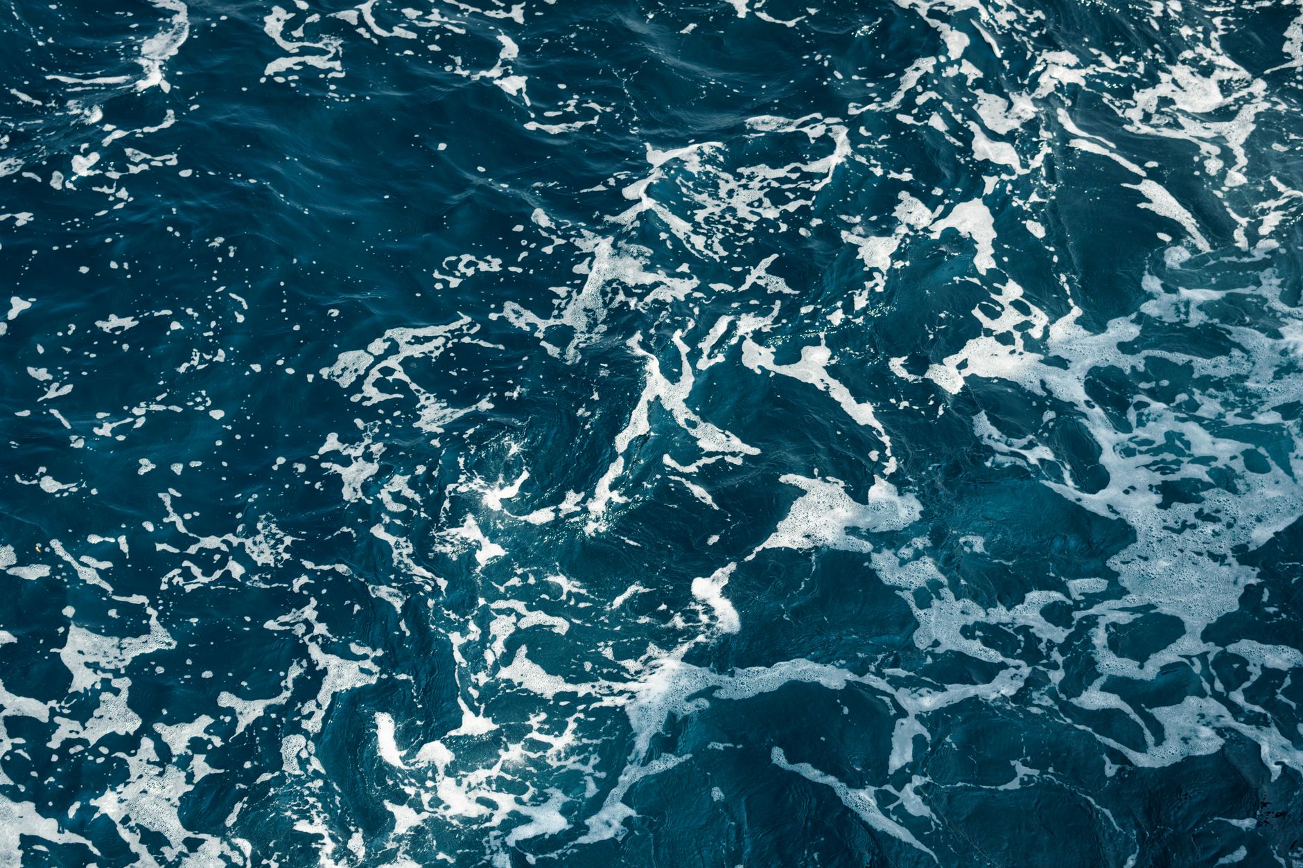 A mesmerizing view of the deep blue ocean with intricate white foam patterns captured from above.