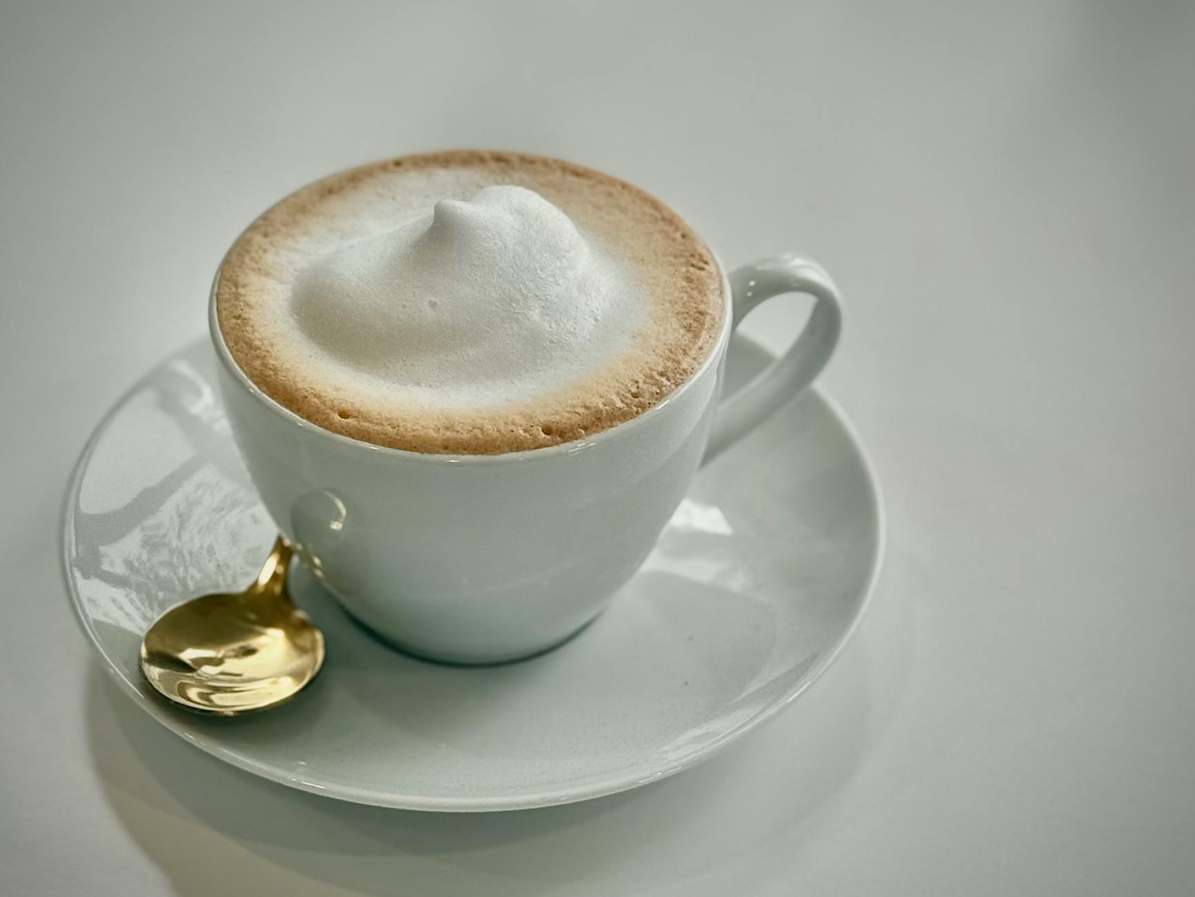 Golden spoon and frothy cappuccino in a white cup create a luxurious coffee setting.