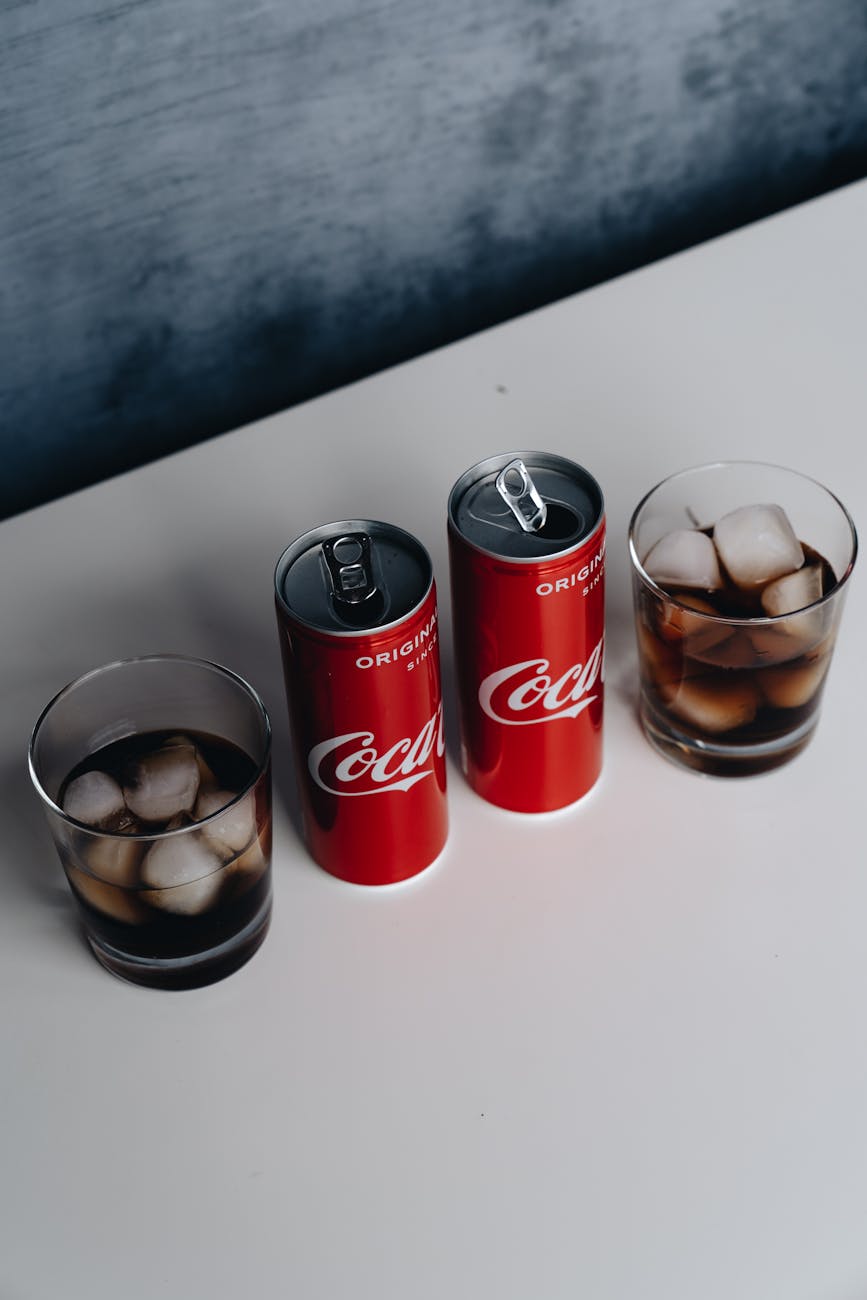 Top view of chilled cola cans and glasses with ice on a white surface, offering a refreshing drink.