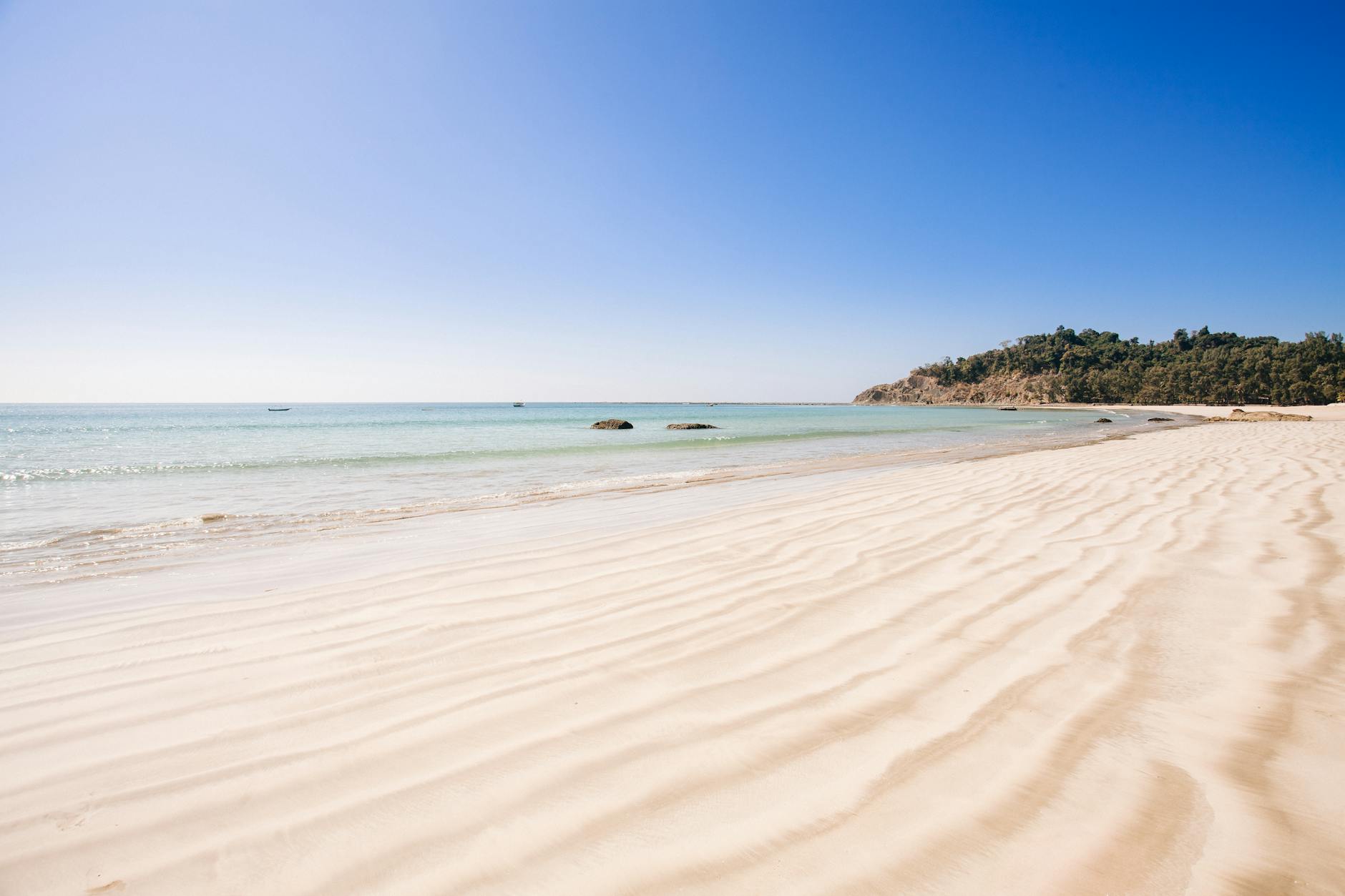 A serene view of a tranquil beach with clear ocean waters and soft sand in Myanmar.