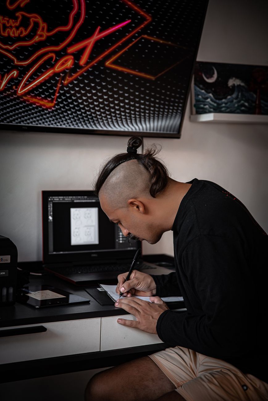 A focused digital artist working on designs in a creative studio environment with neon signage.