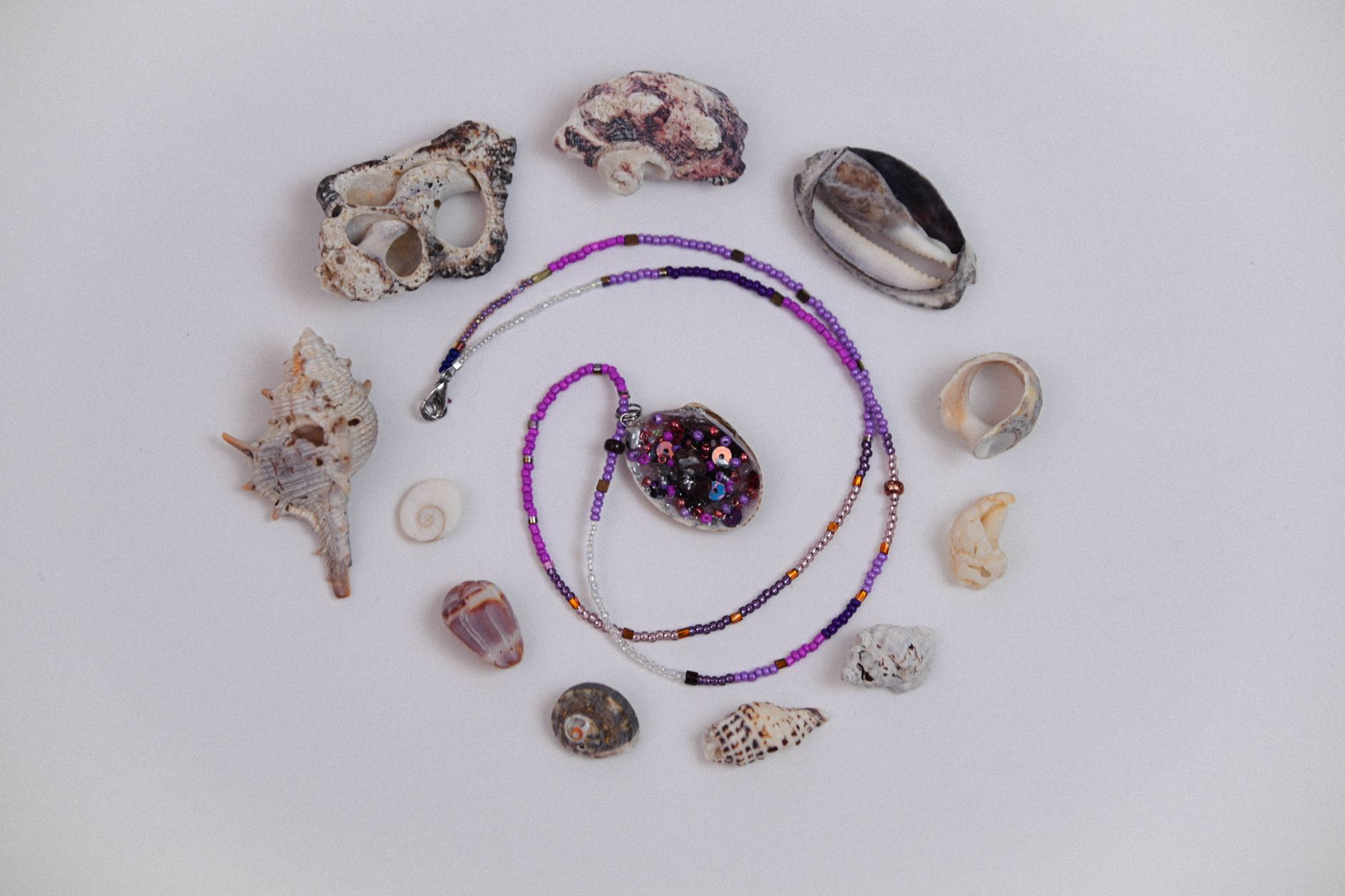 Handcrafted pendant necklace encircled by diverse seashells against a minimalist background.